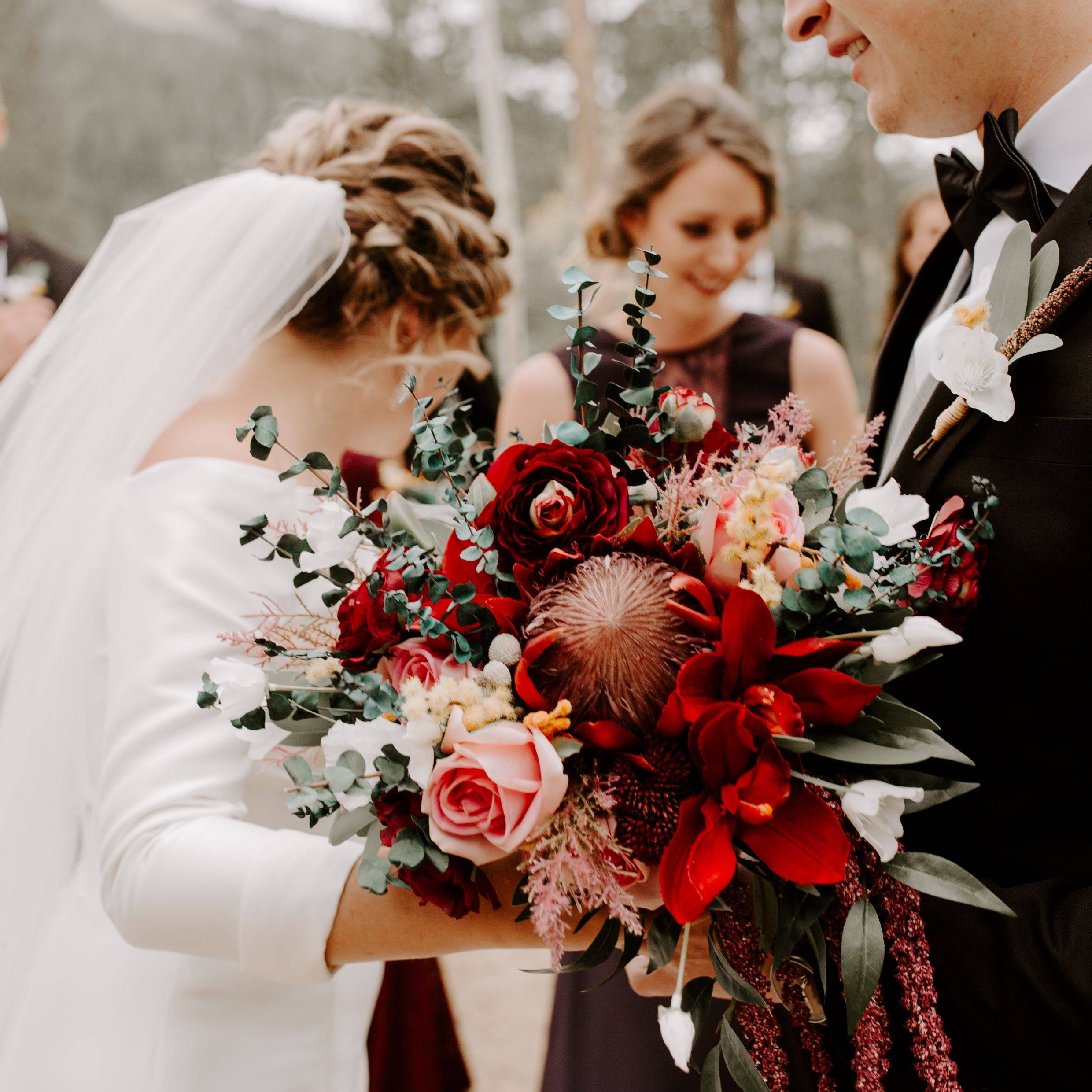 Burgundy bridal bouquet with burgundy protea, burgundy ranunculus, pink roses, and eucalyptus 