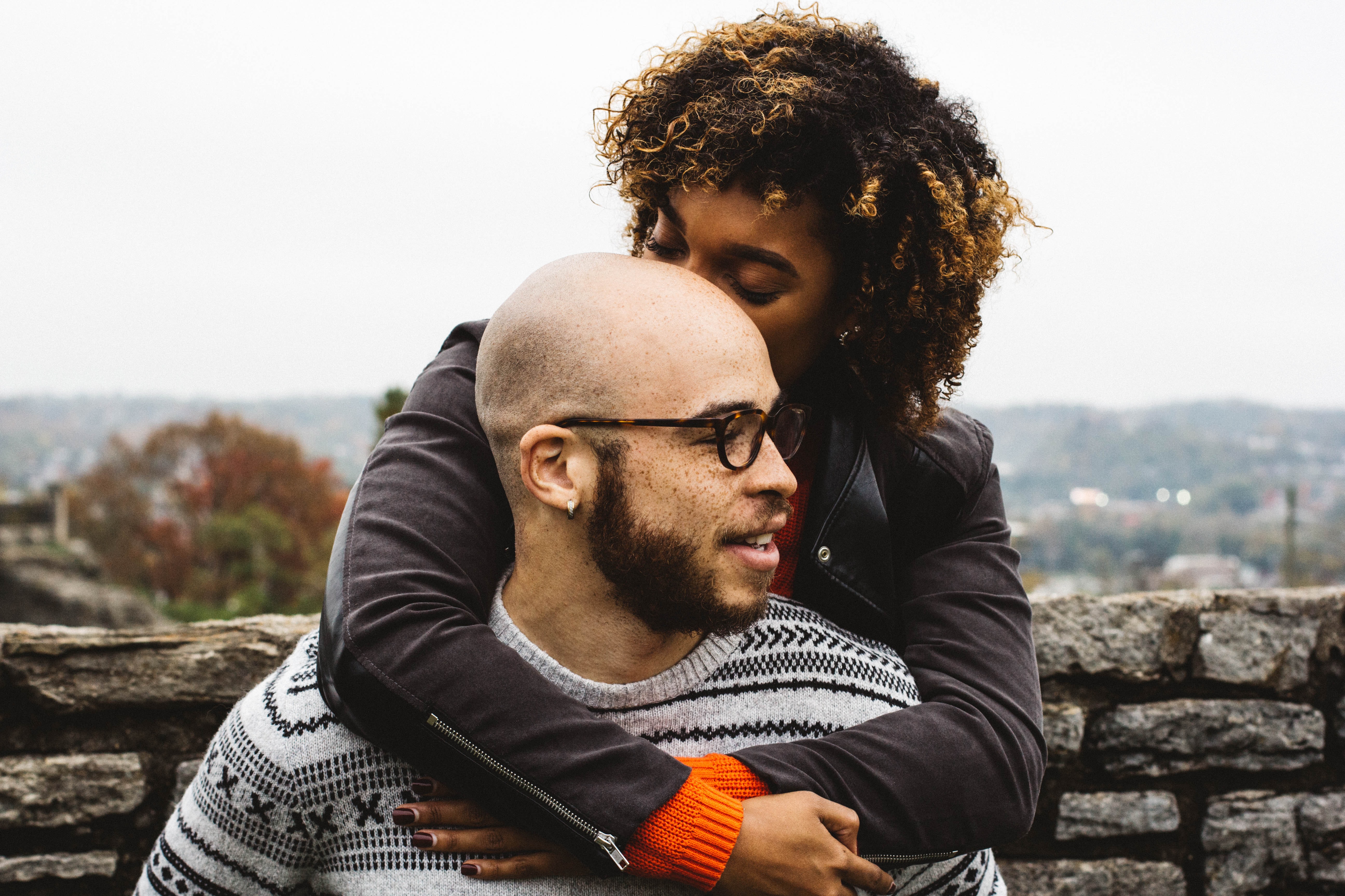 A woman on a man's back, they are both wearing warm clothing and smiling to eachother.