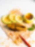 Close-up of a fried fish slice on parchment paper, garnished with fresh lemon slices, chili pepper, and a small bowl of sauce, showcasing a spicy Indian seafood dish.