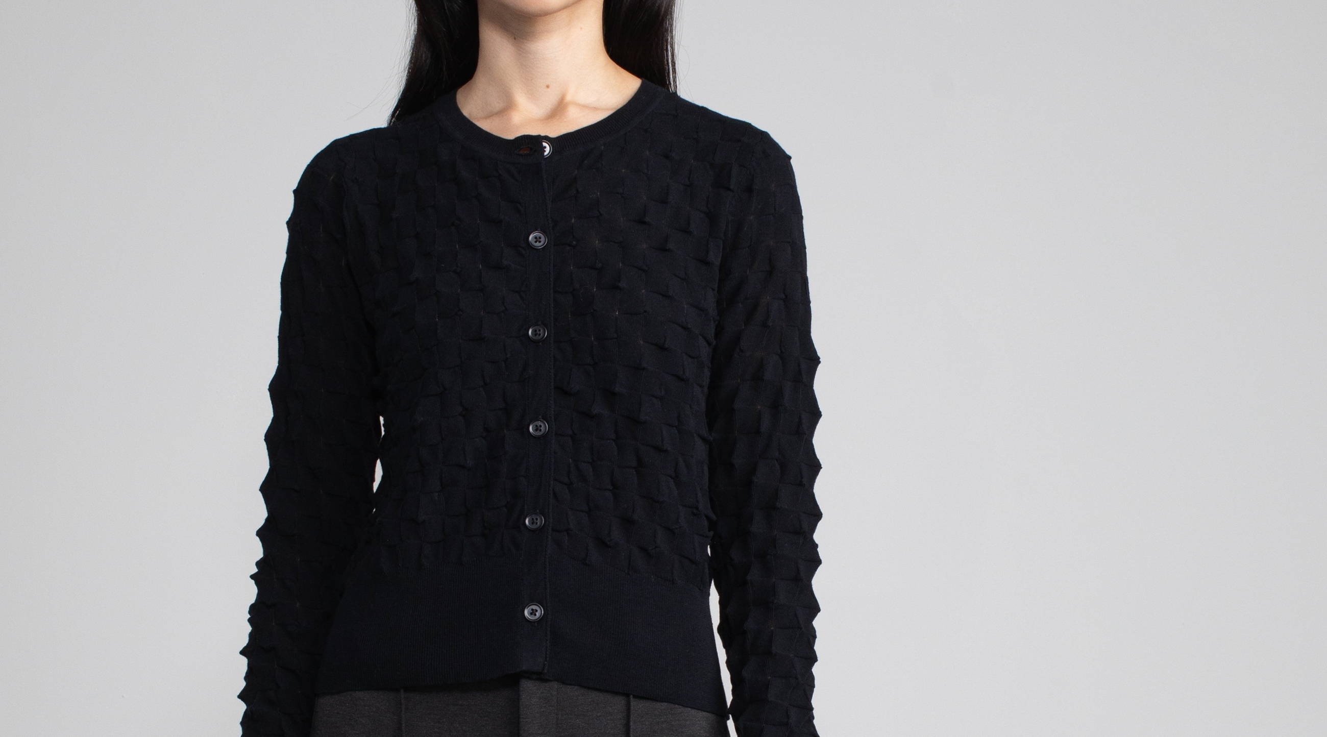 Close up image of a black origami knit cardigan modeled on a woman.