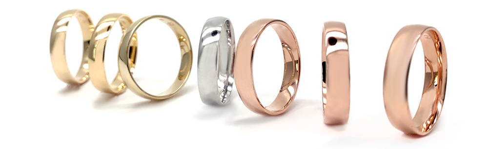 Artistic photo of a series of 7 gold men's bands, three in yellow gold, one in white gold and three in rose gold in the foreground.