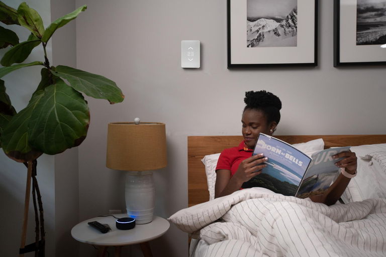 woman reading in bed giving vocal commands to smart home assistant