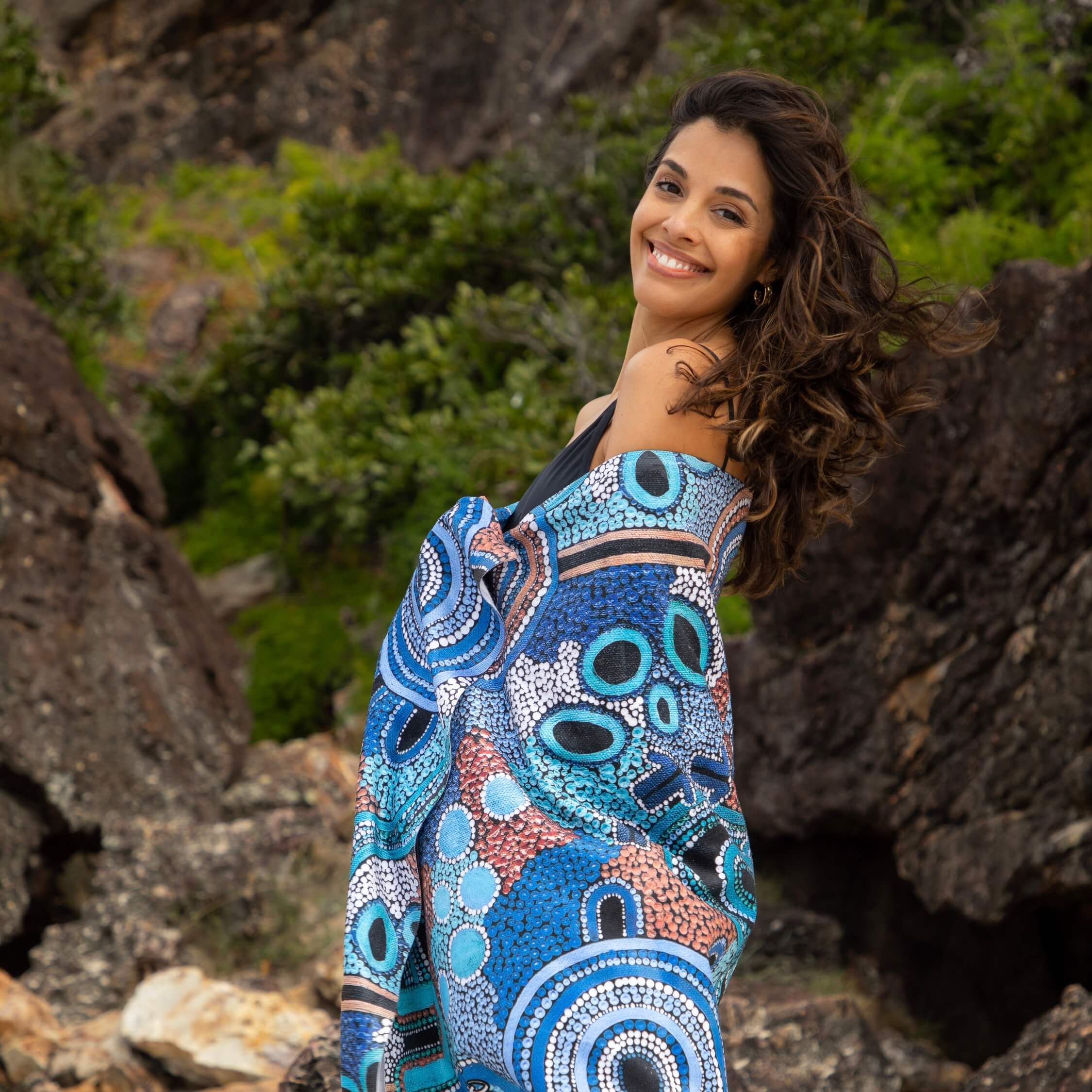 Woman in dress with Aboriginal art holding a gift next to a Christmas tree