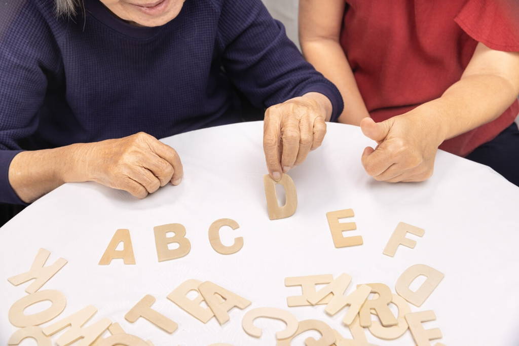 Grandmother teaching her grandson alphabet with thin wooden letters.