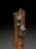 Exquisite drop earrings featuring pear-shaped emeralds and diamond clusters, displayed on a rustic wooden branch against a dark backdrop.