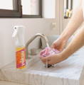 A man is seen running a pink microfiber cloth under a tap in front of a marble sink, with a spray bottle of YOKUU's bathroom cleaner beside it. The sink area is well-lit by natural light coming from a nearby window.