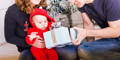 Baby reaching for a wrapped gift while parents hold the present during a family celebration at home.