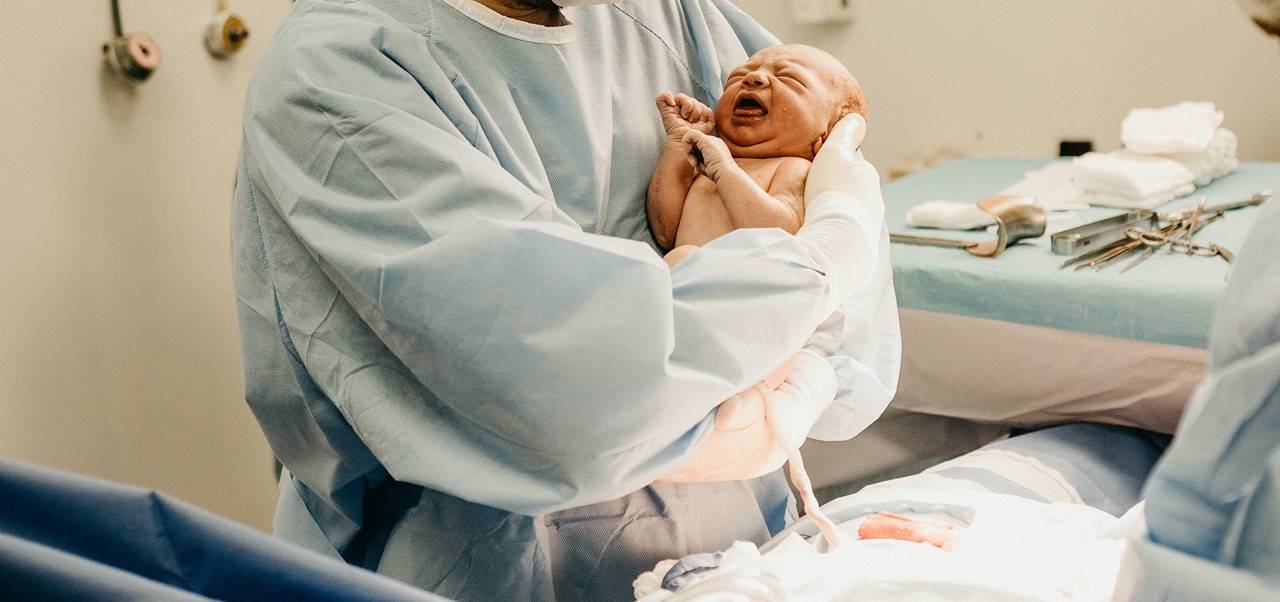 Arzt hält Neugeborenes im Kreissaal in den Armen