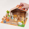 Woman's hand placing a roof on the Montessori Nativity Scene set barn, with wooden figurines visible below.