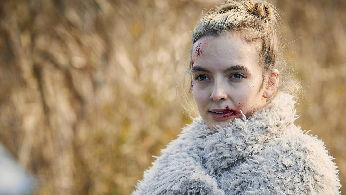 Villanelle talking to Eve in a field. She has on a coat and is bloodied.