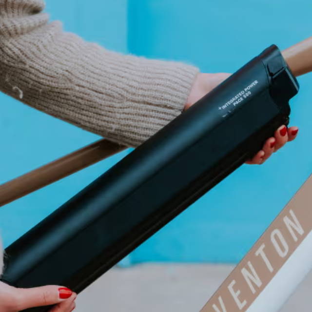 a woman putting an electric bike battery into an aventon pace electric city bike
