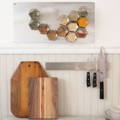 A brightly lit kitchen with two wooden cutting boards, a magnetic knife rack, and a set of magnetic spice jars attached to a metal backsplash