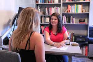 Dr. Keila Roesner, ND MSCP, consults with a patient in a cozy office filled with books and wellness products.