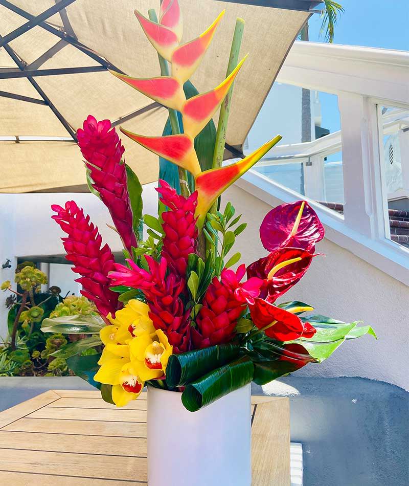 Arrangement of tropical flowers in reds and oranges, placed on a table under an umbrella