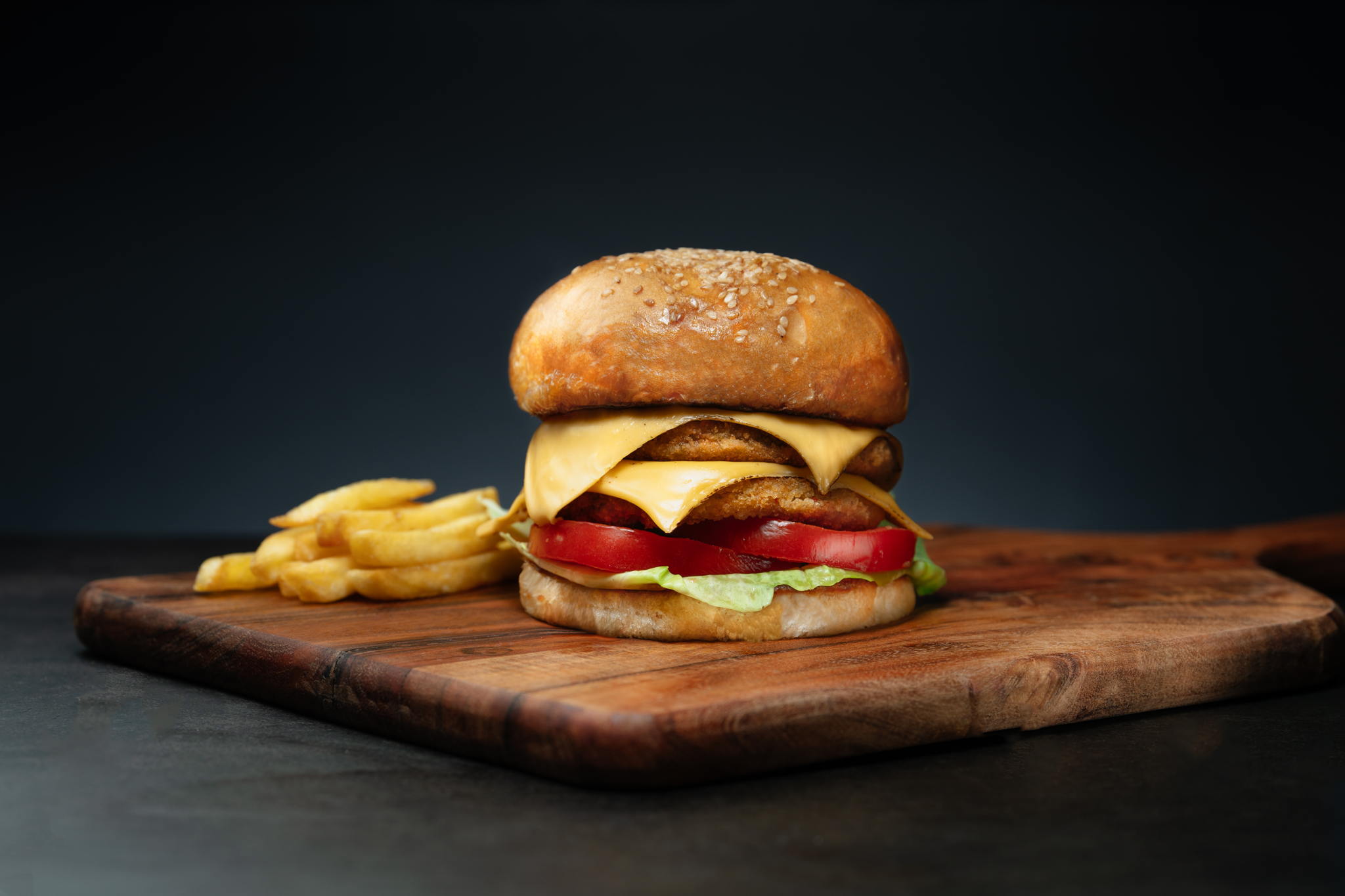 A juicy cheeseburger on a wooden cutting board, served with a side of golden french fries