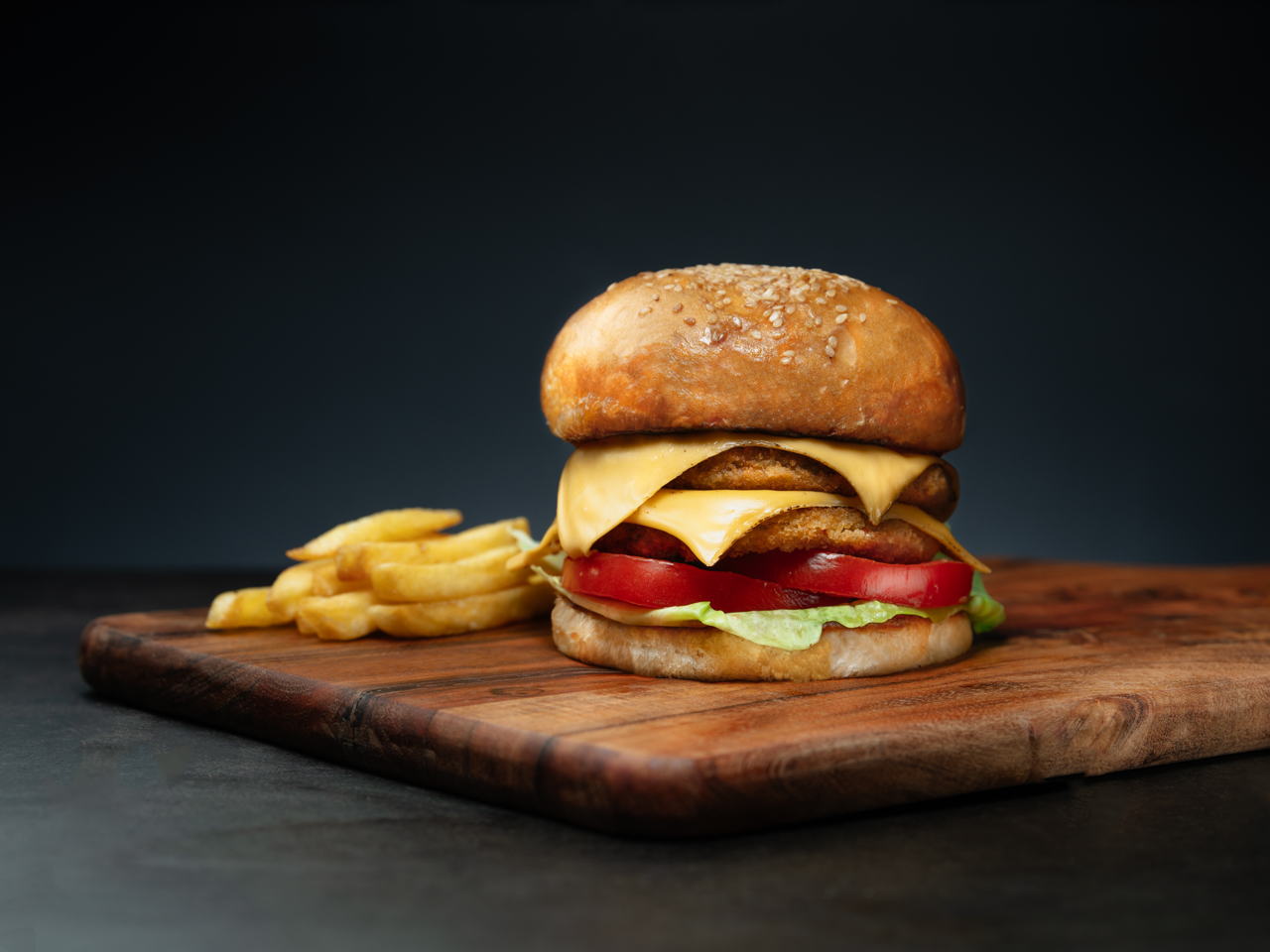 A juicy cheeseburger on a wooden cutting board, served with a side of golden french fries