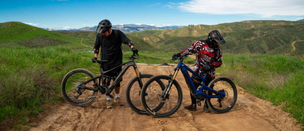 two people standing next to thier full suspension electric mountain bikes in the wilderness
