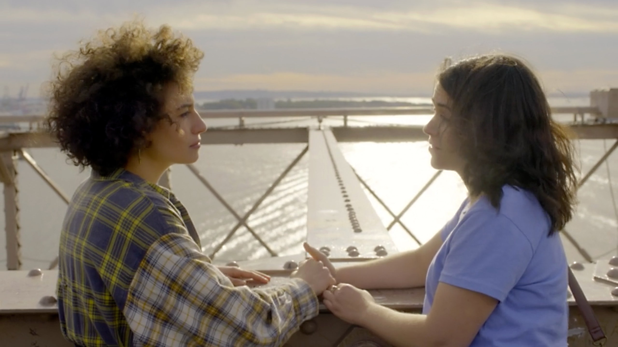 Ilana and Abbi holding hands talking on a bridge while overlooking a river.