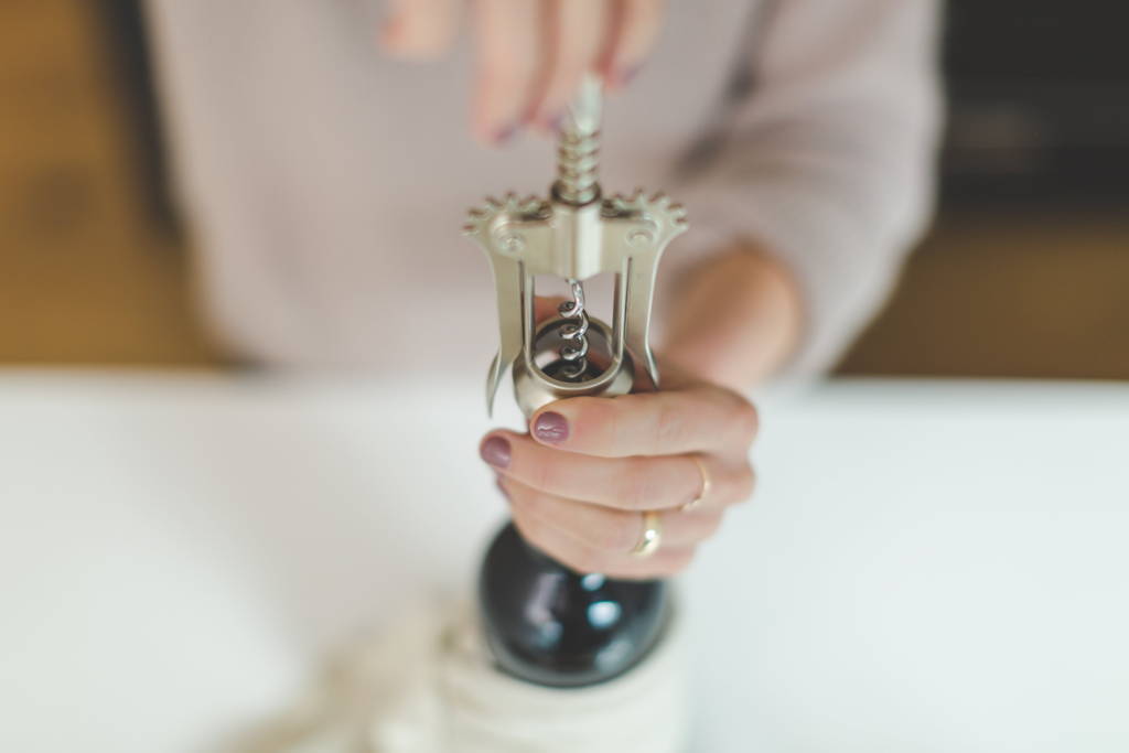 Woman in action using bottle opener to remove cork from a bottle of red wine allowing wine to aerate.