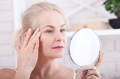 woman looking in the mirror at her wrinkles and fine lines
