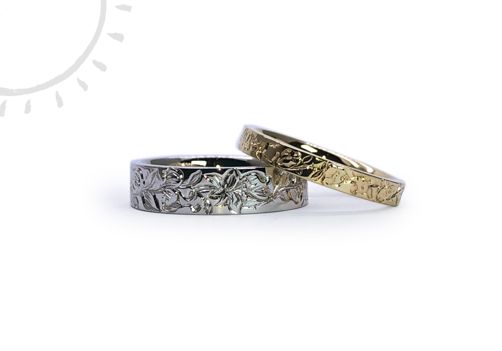 A pair of wedding rings with handmade flower engravings in white gold for men and yellow gold for women.