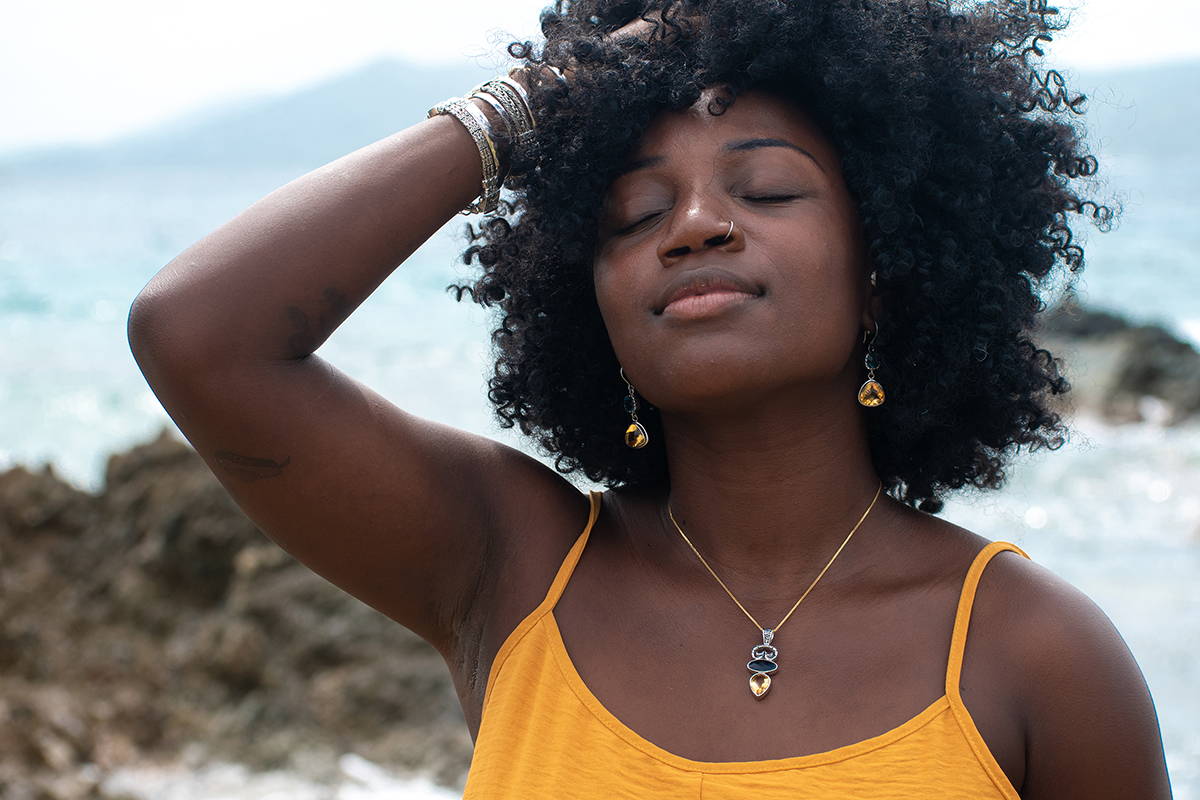 A woman standing next to the ocean surf wears pendants and chains.