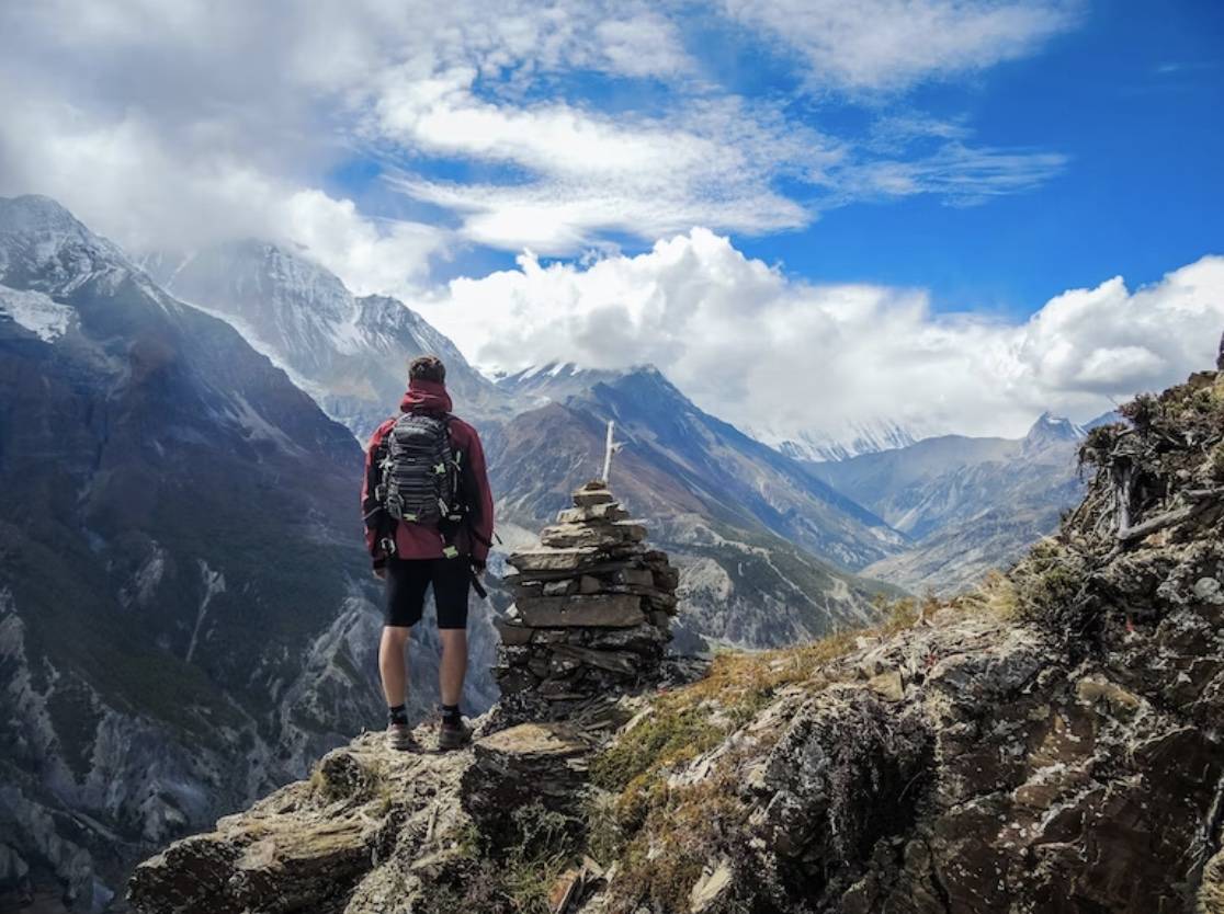 Man standing on the top of a mountain beside cairn stones