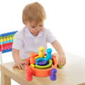 A boy sitting on a chair and holding a green peg while playing with a colorful Montessori Rainbow. 