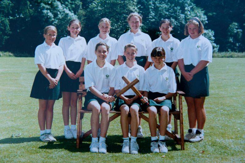 A team of school girls including a young Kate Middleton poses in front of a green field. They are in uniform and holding athletic equipment.