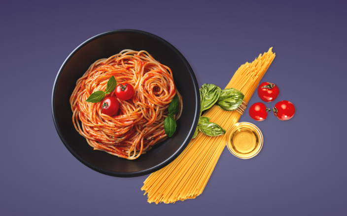 A plate of spaghetti next to a bundle of pasta, basil, and tomatoes for Confetti's Virtual In Home Cooking Classes