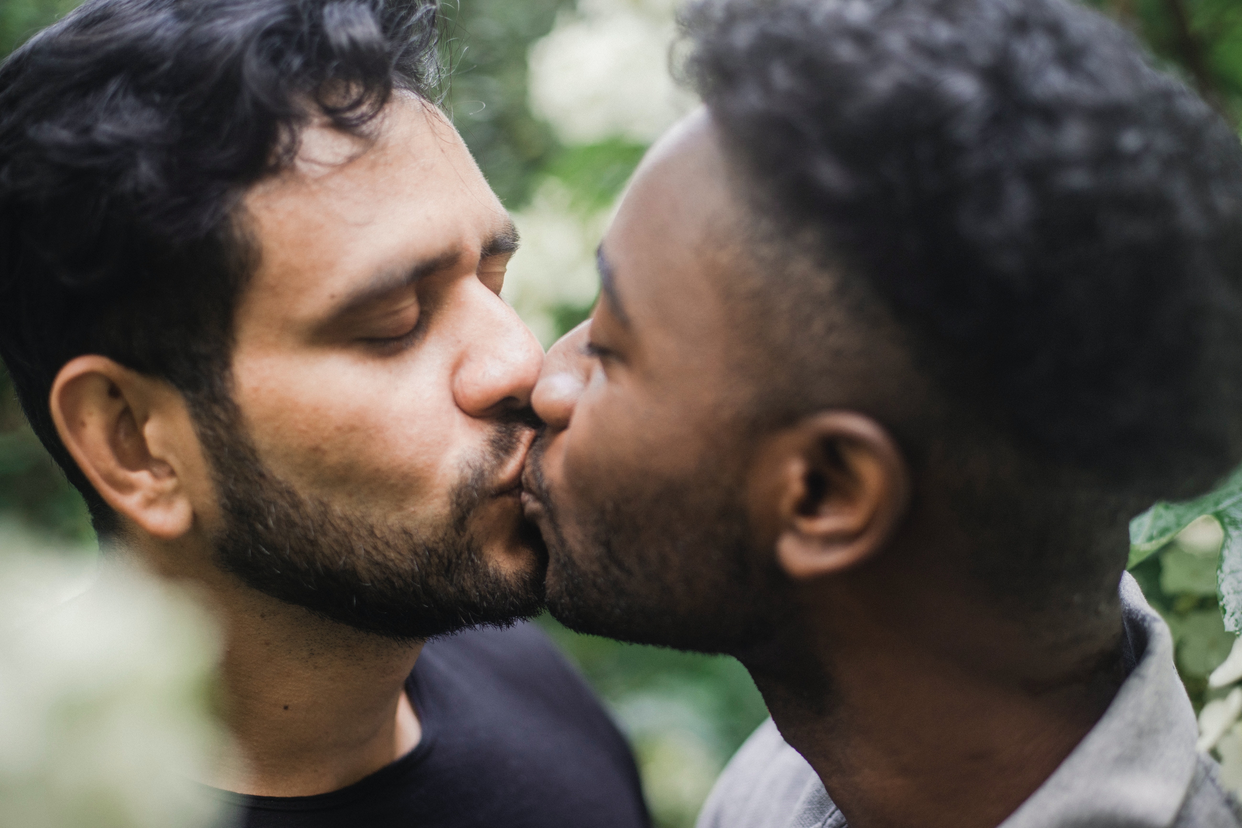 Two men share a kiss in the outdoors. 