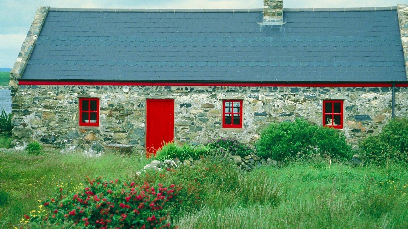 Irish stone cottage with red doors set amongst green grass and wildflowers in countryside