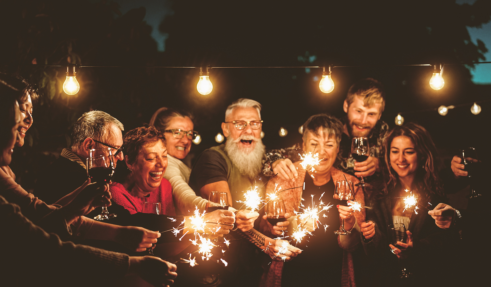 A large family of different ages laugh together holding sparklers during the night.