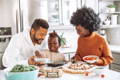 Mother, father, and toddler making pizza in the kitchen.