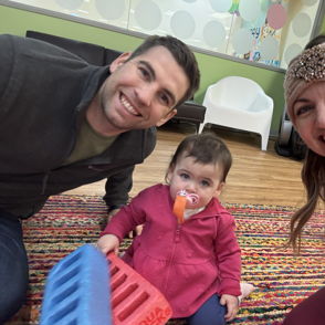 A joyful family moment: a man and woman smile at the camera, while a young girl in a pink jacket sits between them.