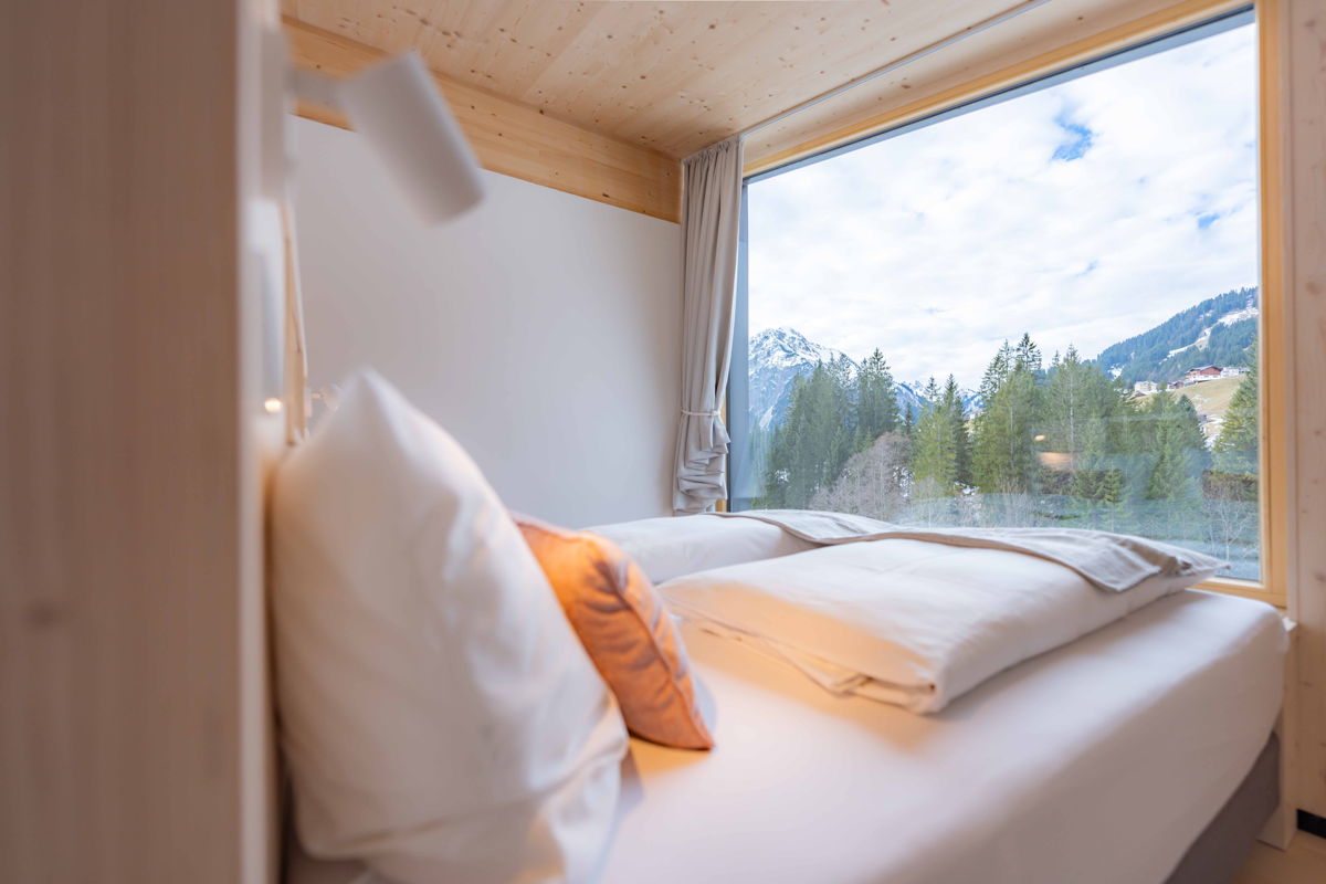 Schlafzimmer mit Doppelbett und Fensterblick auf die Berge im Apartment Hochsitz von Hugo & Pepi in Mittelberg im Kleinwalsertal.