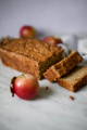 Spiced apple cake is cut into slices with a few loose apples spread around it