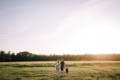 Babymoov Lifestyle image, a family of three walking in a large green field during sunset