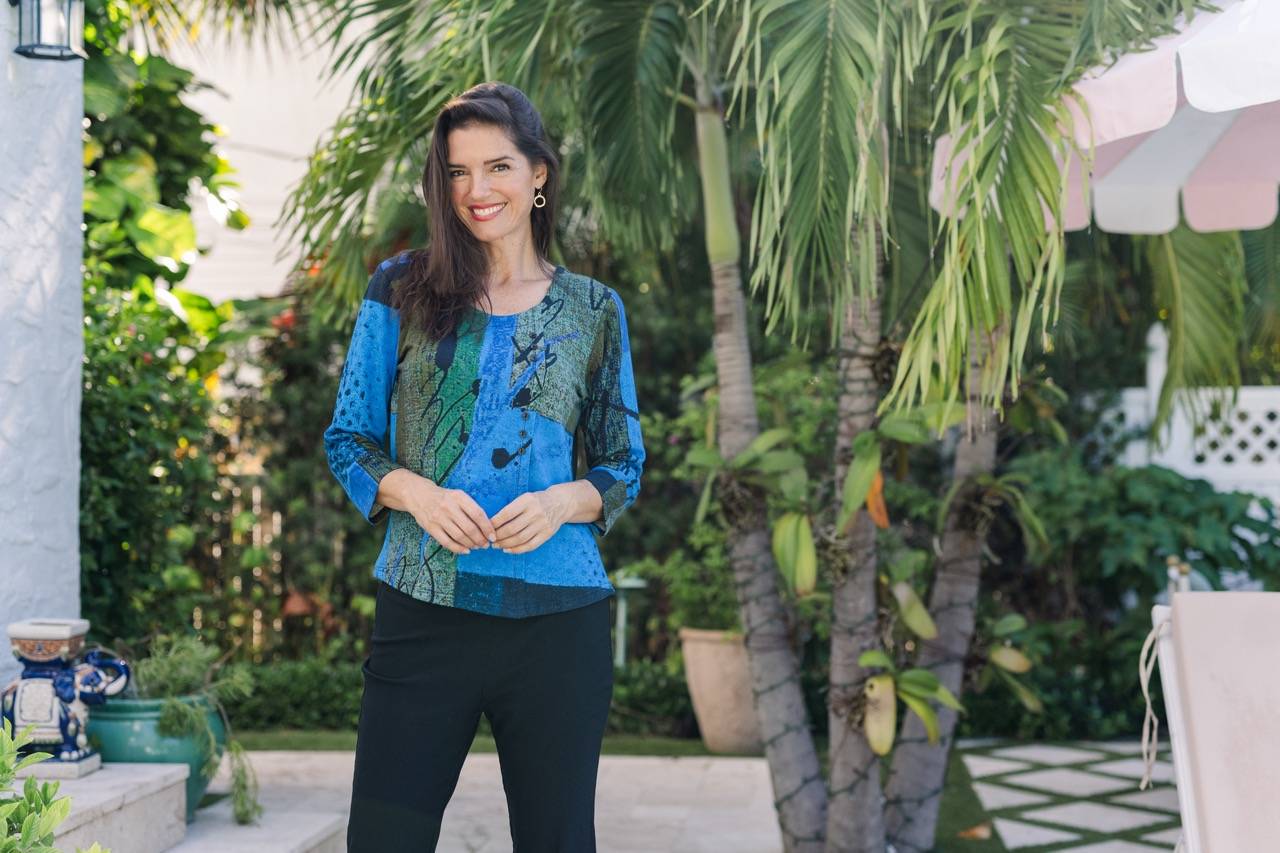 A woman wears a blue offset button pocket top in a lush yard.