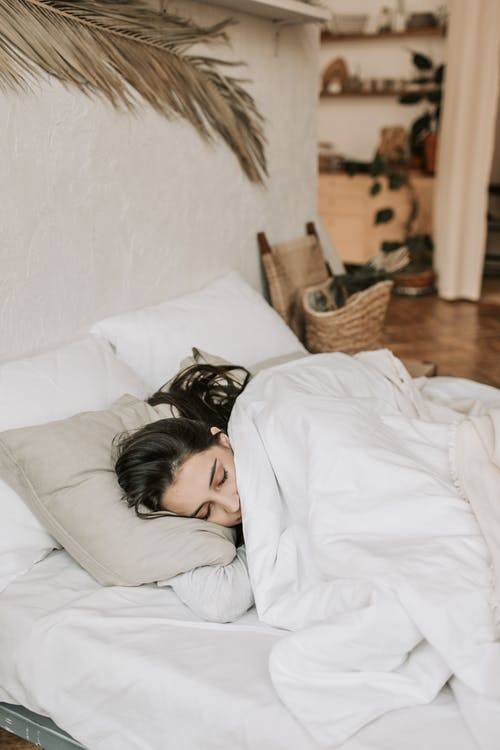 girl sleeping under blanket on white bed sheets
