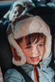 A smiling brown haired child wearing a sheepskin hat