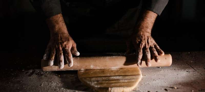 Mains d'artisan basque abaissant une pâte au rouleau