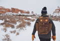 a person wearing a summit expedition pack walking through a snowy desert with rock formations in the background