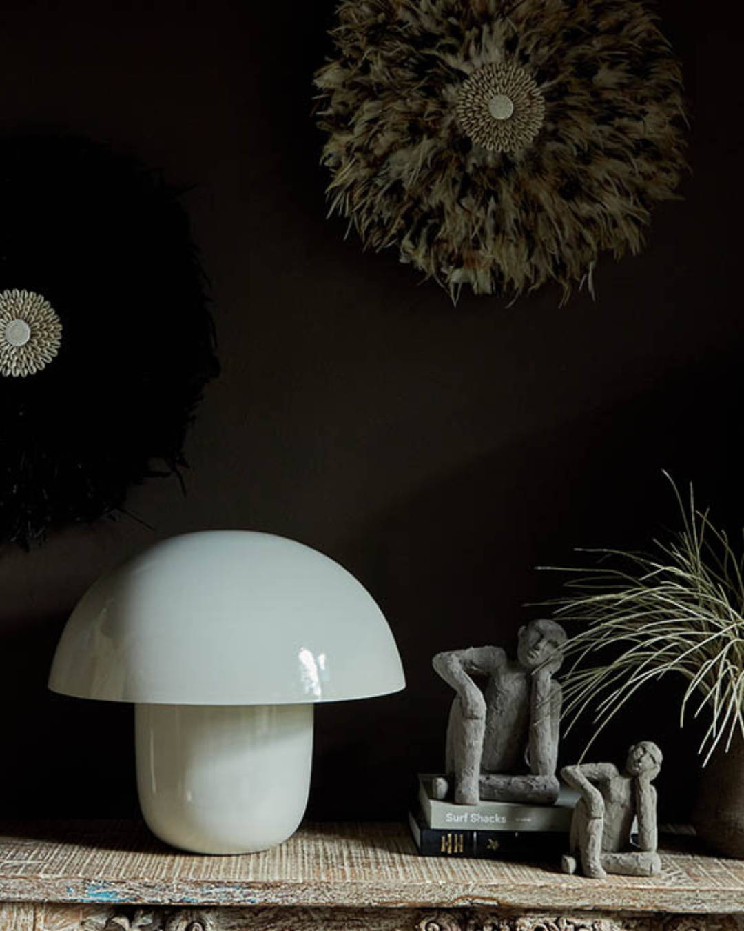 a dark painted wall with a white curvy lamp next to some male sculpture in thoughtful pose resting on some books