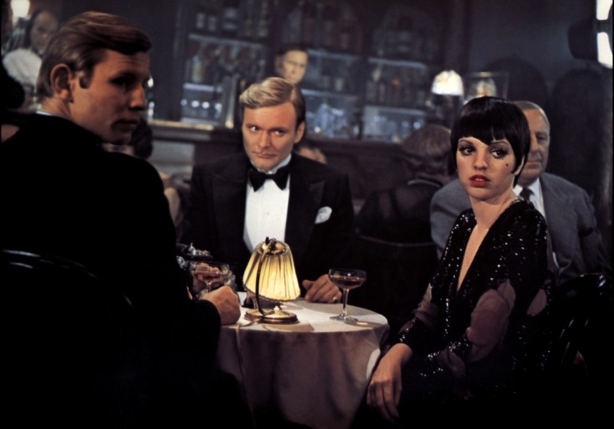 Max Sally and Bryan dressed up, sitting together at a nightclub table, all turned towards someone off camera.