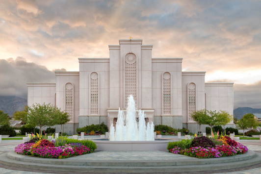 Albuquerque Temple with a water fountain in front of the entrance.  The flowerbeds are full of colorful flowers.