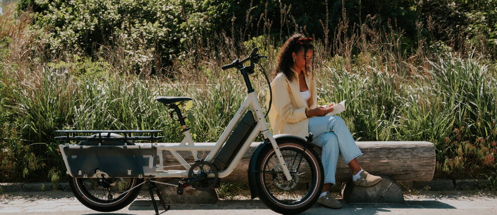 a woman sitting next to a white Specialized Globe Haul electric long haul cargo bike