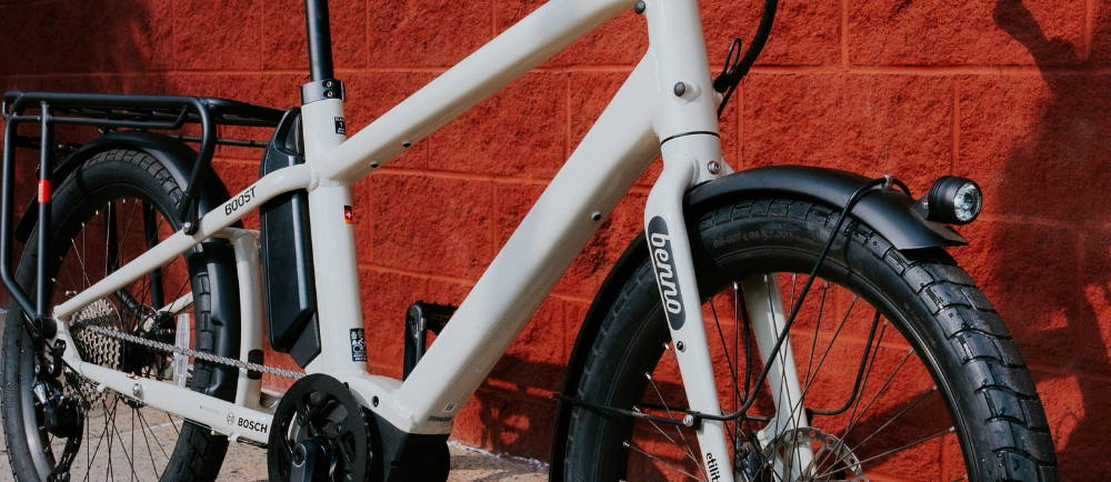 a white Benno Boost longtail electric cargo bike against a brick background