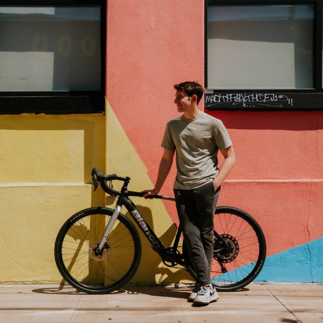 a man standing next a Bianchi E-Impulso electric road bike in front of a yellow and peach colored wall