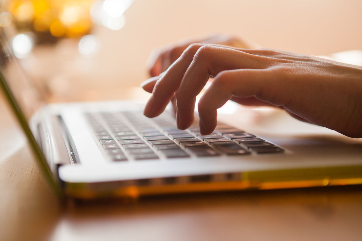 Close-up of a persons hands typing on a laptop keyboard, with warm light illuminating the scene and creating a soft, focused atmosphere.